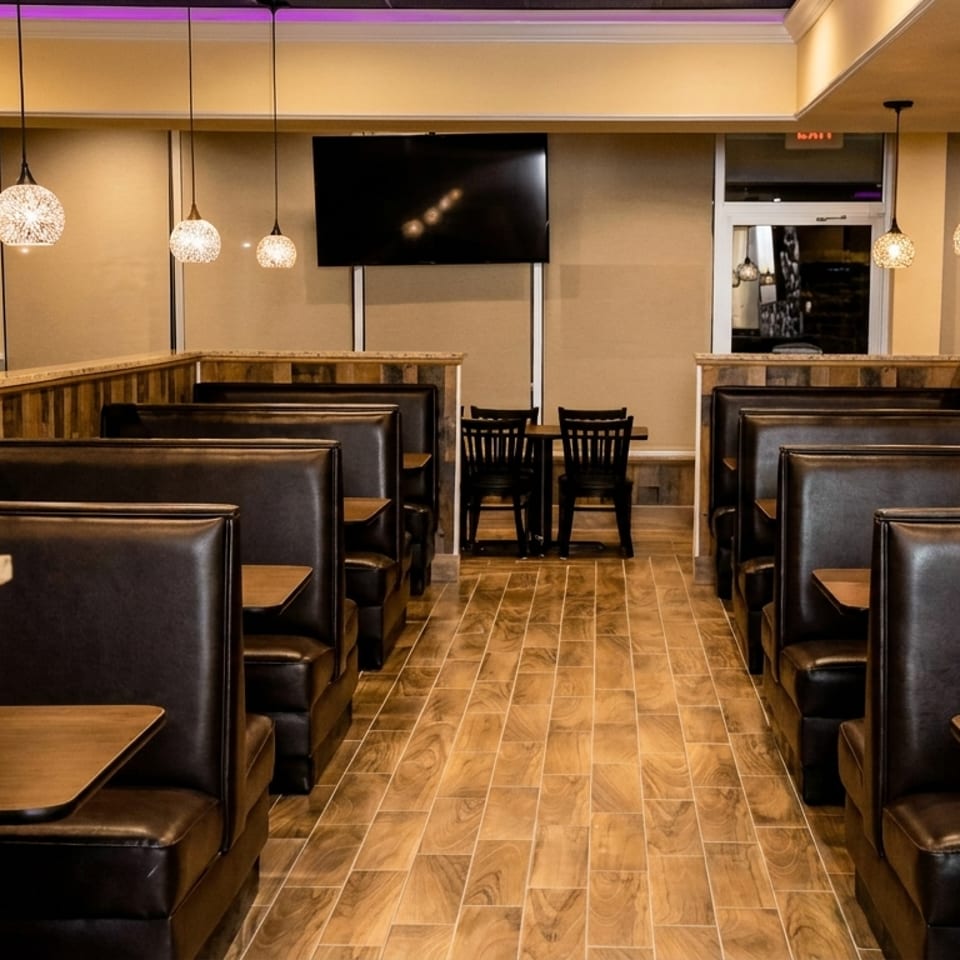 Warmly lit restaurant dining area with dark leather booths, wooden floors, pendant lights, and a wall-mounted television.