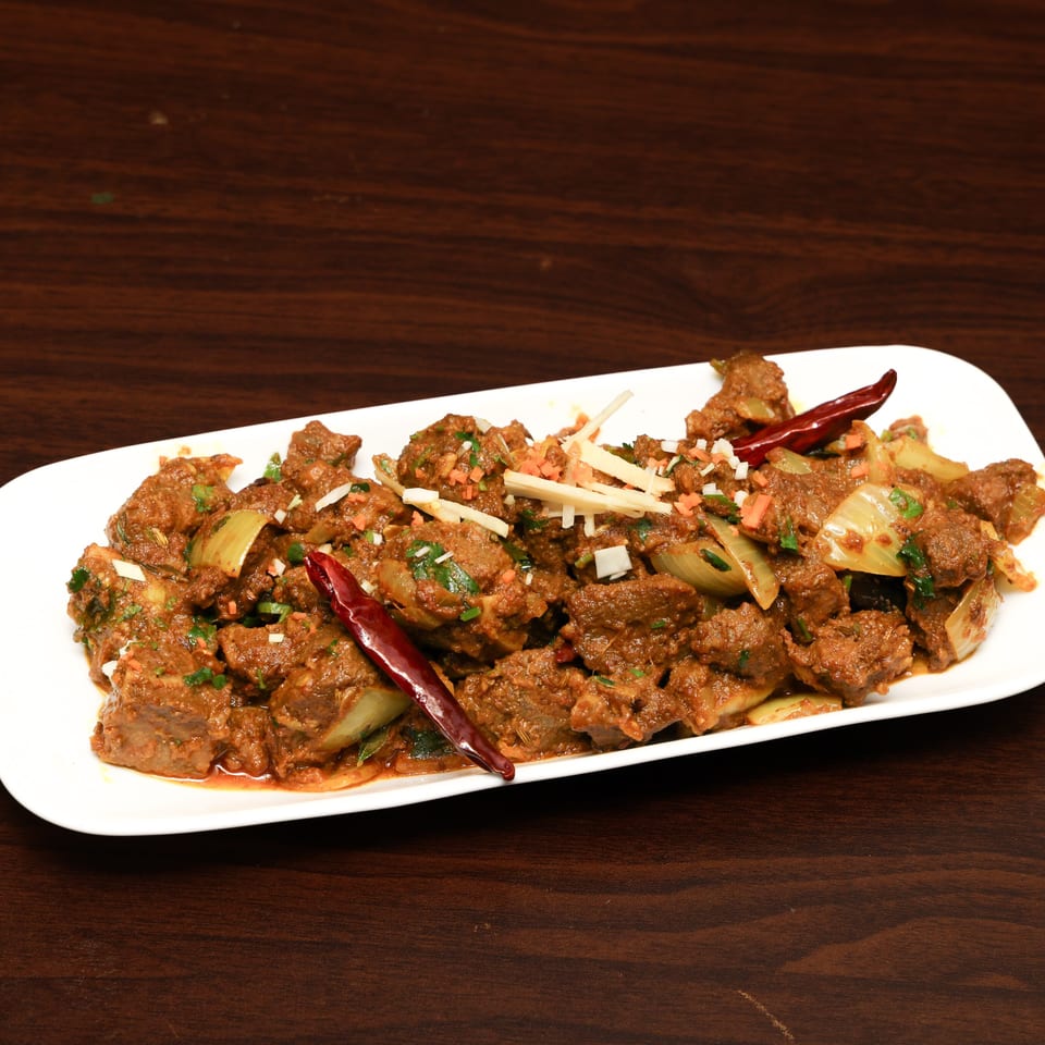 Spiced meat curry with onions, herbs, ginger, carrots, and dried red chilies served on a white platter.