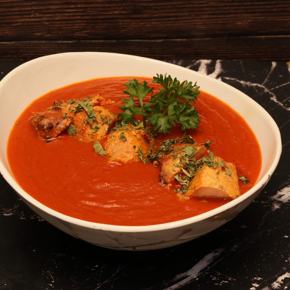 Bowl of creamy red tomato sauce topped with grilled chicken pieces, dried herbs, and fresh parsley on a dark marble table.